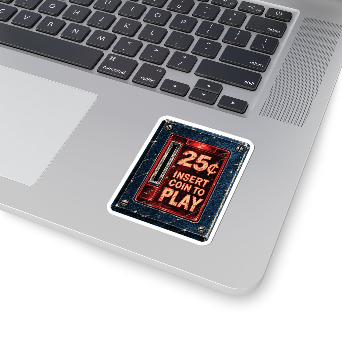 3 by 3 inch retro arcade coin door sticker applied to a laptop beside the keyboard