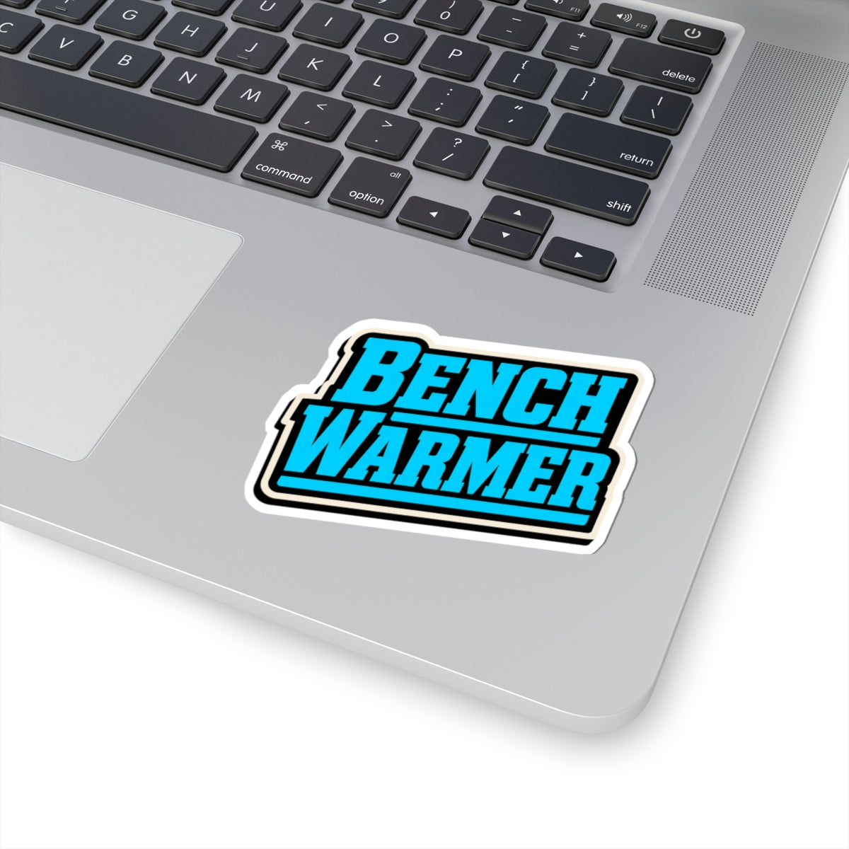 Bench Warmer kiss-cut sticker on a laptop keyboard — retro sports graphic sticker applied to silver MacBook