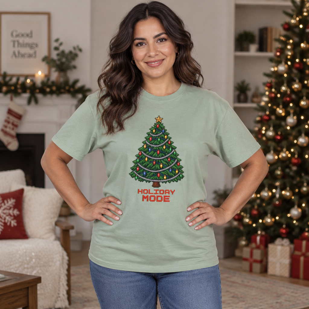 Woman with long dark wavy hair wearing a Bay sage green Holiday Mode pixel Christmas tree tee in a decorated living room