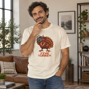 Smiling man with curly dark hair wearing an Ivory cream Jive Turkey pixel turkey tee in a living room with a leather couch