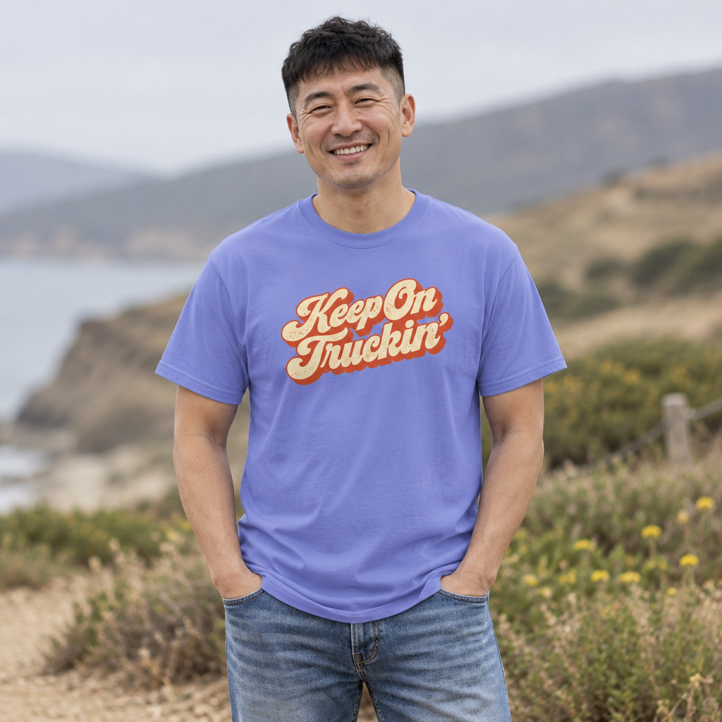 Smiling man wearing the Flo Blue Keep On Truckin' graphic tee on a coastal hillside trail