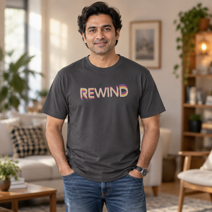 Man with dark wavy hair wearing the Graphite Rad Rewind REWIND tee in a sunlit living room