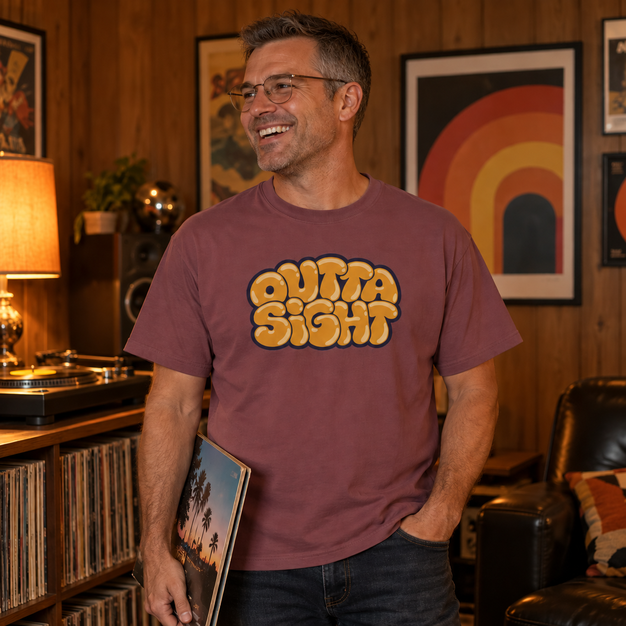 Laughing man in glasses wearing the Brick Outta Sight graphic tee in a wood-paneled rec room with a turntable