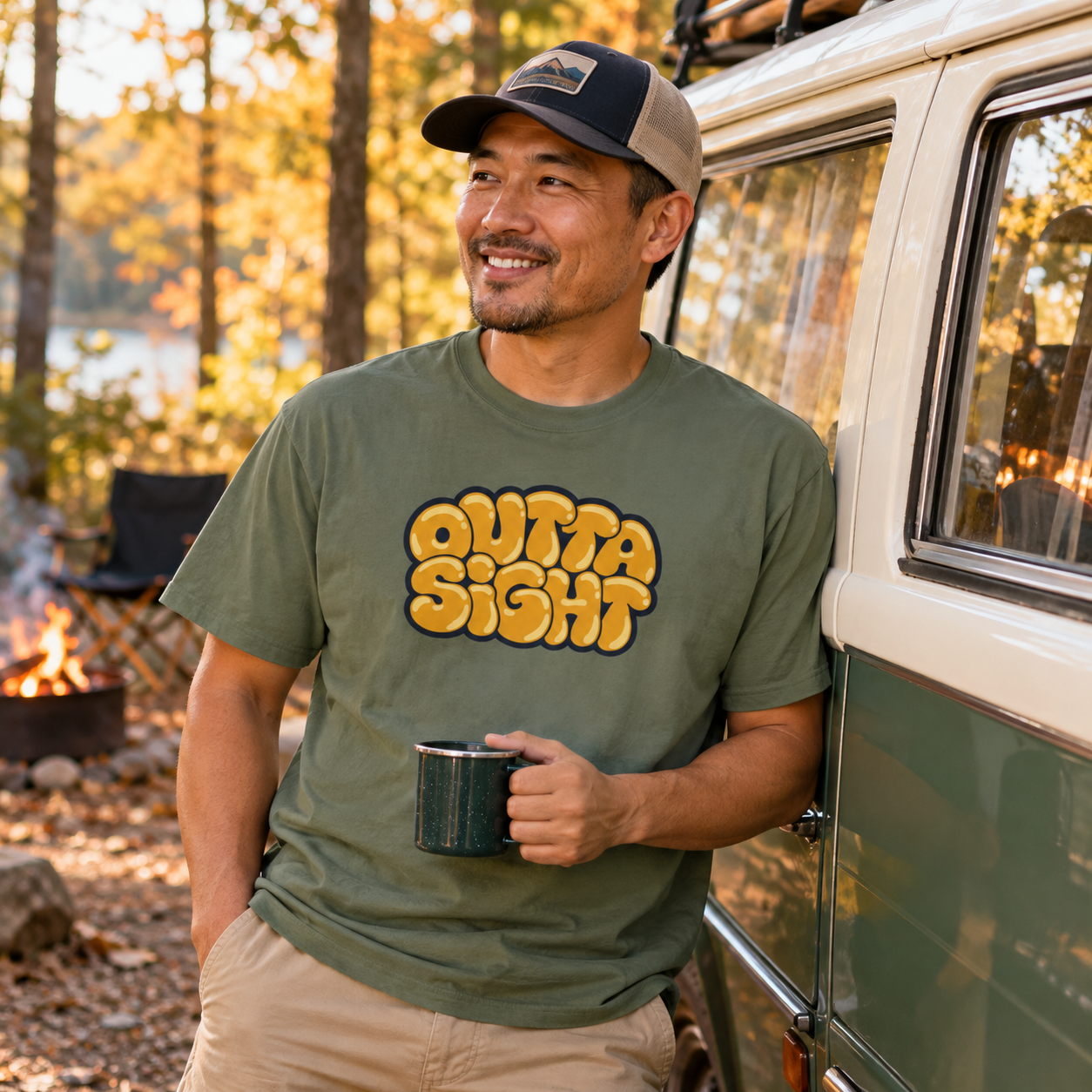 Smiling man in a ball cap wearing the Moss Outta Sight graphic tee beside a retro camper van at a fall campsite