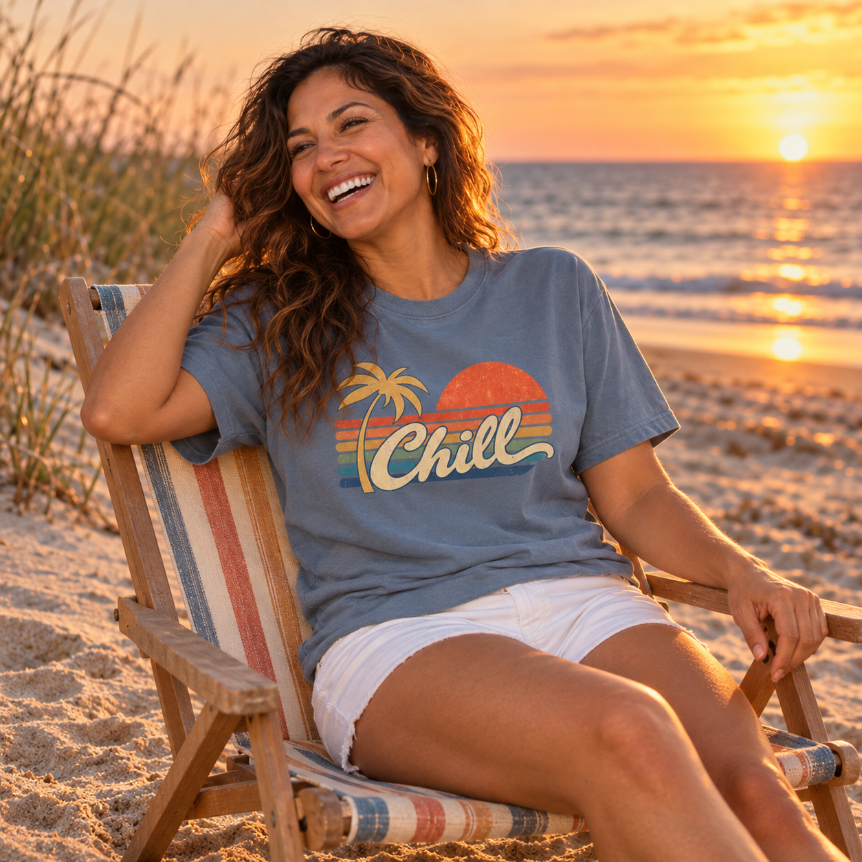 Laughing woman in a striped beach chair at sunset, wearing the Blue Jean Chill graphic tee