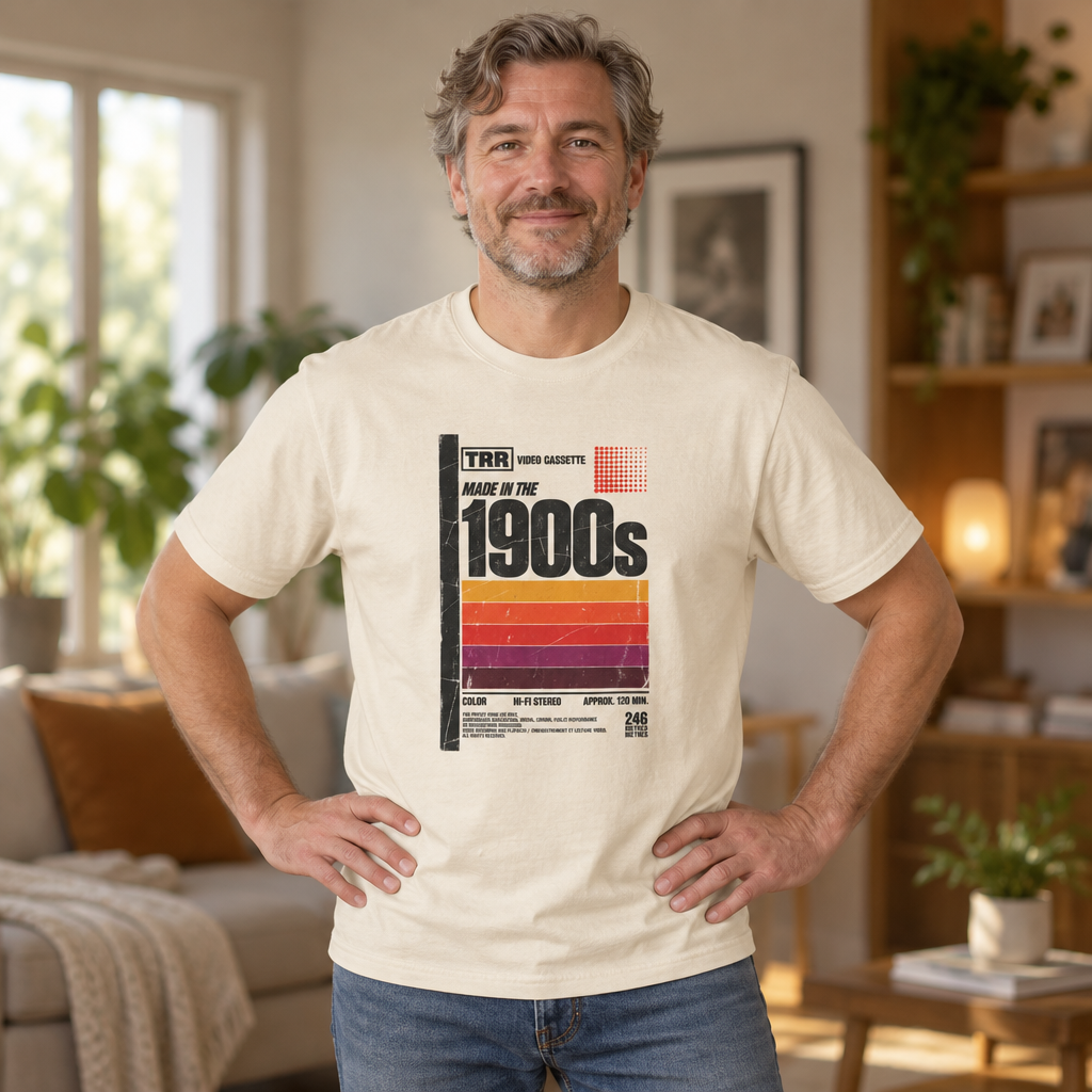 Cream retro VHS tee with “Made in the 1900s” and sunset stripes, worn by a man in a cozy living room.